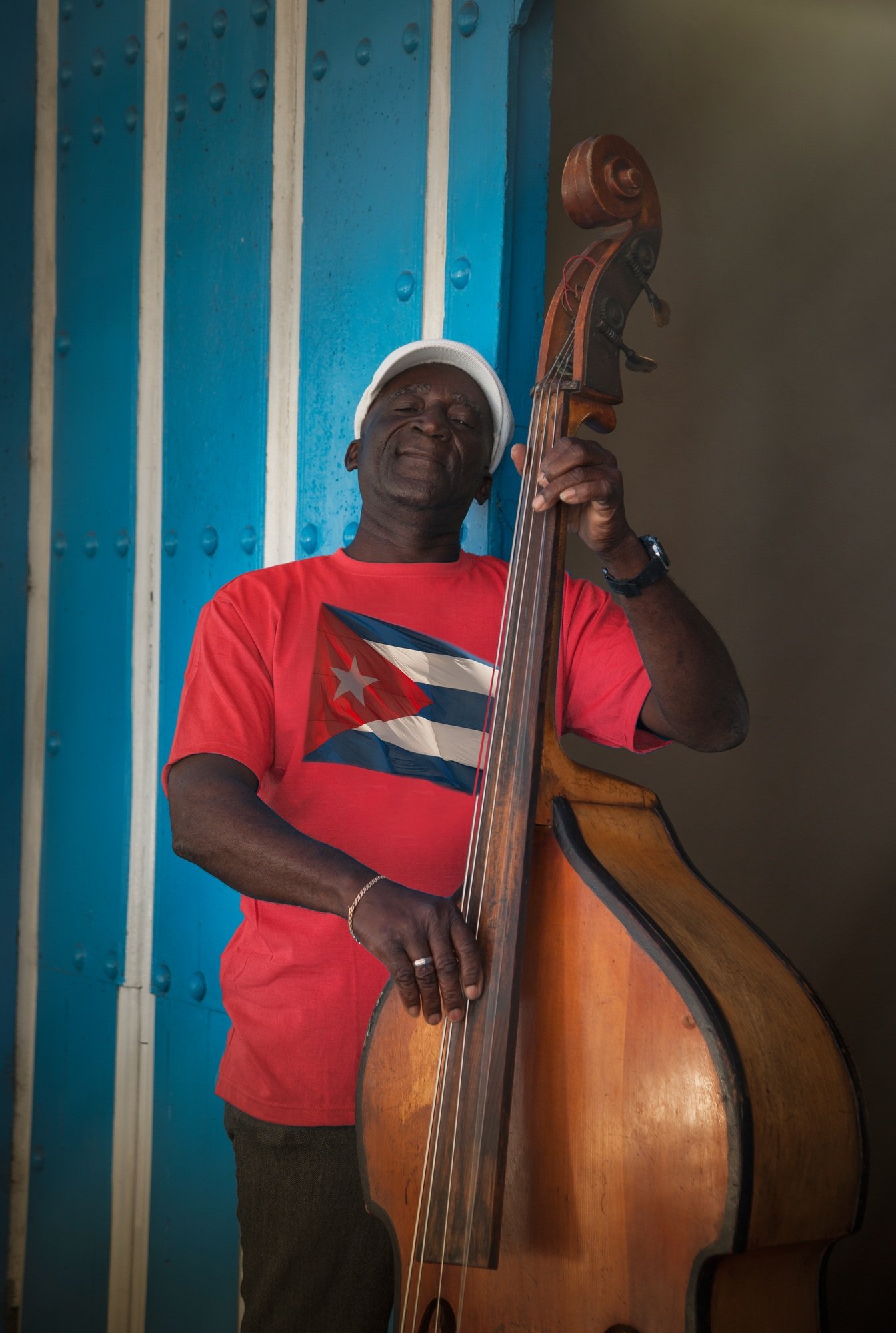 Senior man playing double bass in front of blue wall, Santiago de Cuba, Cuba